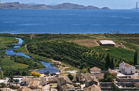 Colour view from Pontinos over the roofs of Myloi, a church with a bell tower, the winding stream of the Lerna springs, the roofed excavation and the Argolic Gulf.