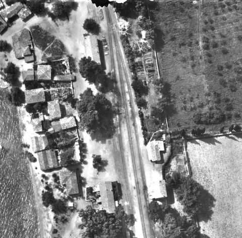 Crop of the 1941 aerial photo of the station core: double track and sidings, a long gabled building by the track with wagons (probably the goods shed), detached tiled buildings opposite, and village houses along the beach.