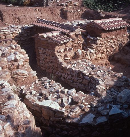 Lerna: the Early Helladic fortification wall (early 3rd millennium BC) topped with mud bricks, under protective roofs, on red earth.