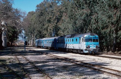 Myloi station yard under eucalyptus trees with blue OSE railcar A.6461, three coaches and a water crane.