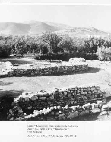 Early and Middle Helladic wall remains at the Lerna excavation from the north, with trees and hills behind.