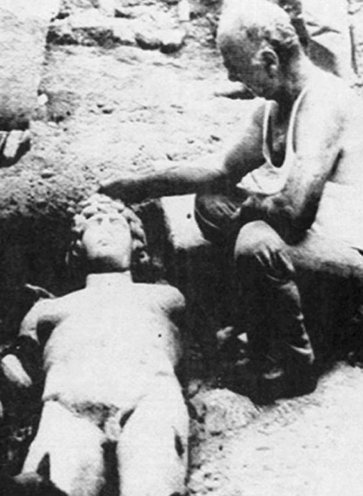 Black-and-white photo from 1986: a man kneels beside the statue of Antinoos, still lying in the ground at Myloi