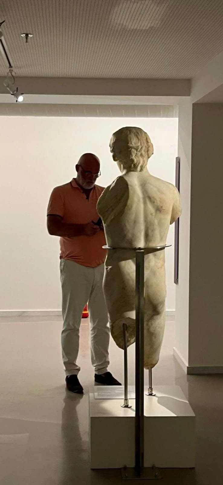 Johan Overtoom, editor of Visit Myloi, with the marble statue of Antinoos, seen from behind, in the museum in Argos
