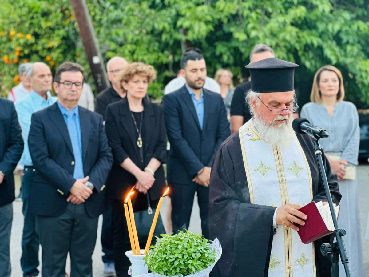 A priest reads the memorial prayer at a microphone, with candles and basil in front of him and guests standing behind, 15 June 2025