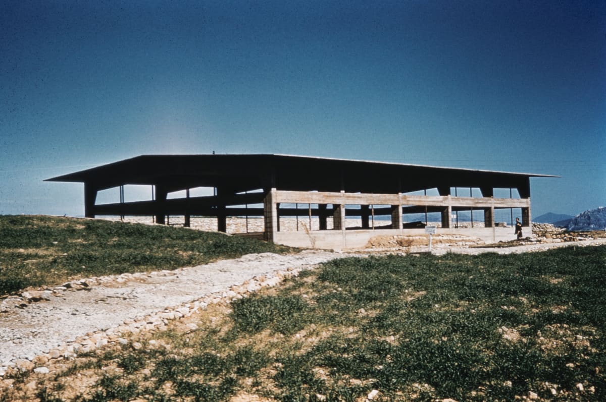 The newly built concrete protective roof over the excavation at Lerna under a deep blue sky, with a gravel path and grass in front, 1950s