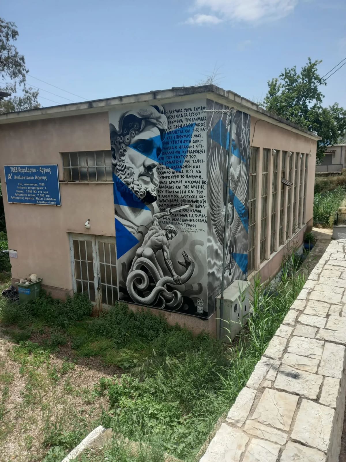 The 1960 pumping station of Lerna on the Argos–Tripoli road in Myloi, with its sign of the Kefalari–Argos irrigation board and the mural of Heracles and the Hydra.