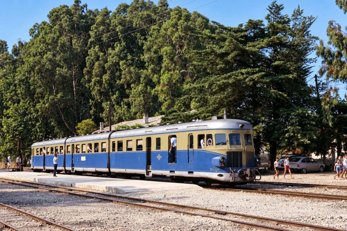 A blue and beige railcar waiting at the platform of Myloi station under tall trees (digitally restored)