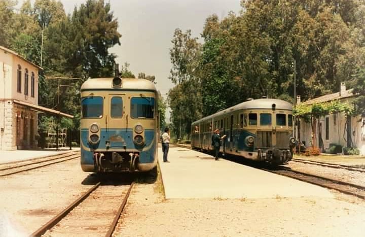 Two railcars side by side at Myloi, with the stone station building on the left