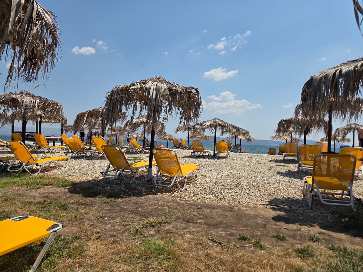 Yellow sunbeds under straw umbrellas on the pebble beach, with the sea beyond