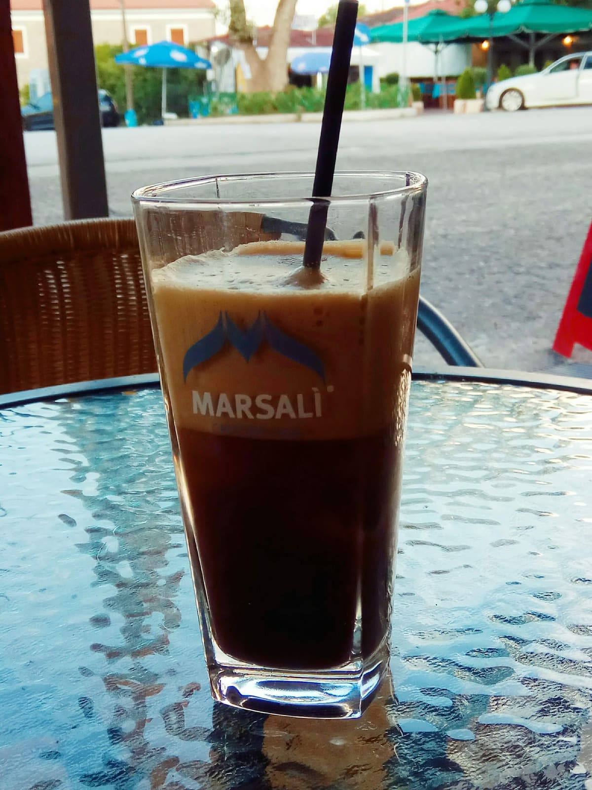 A tall iced coffee with a straw on a terrace table