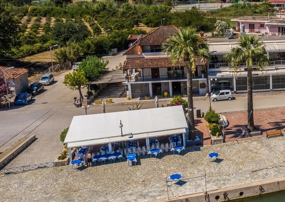 Faros from the air: the covered terrace and blue tables on the paved quay by the water, the house across the road and two tall palm trees