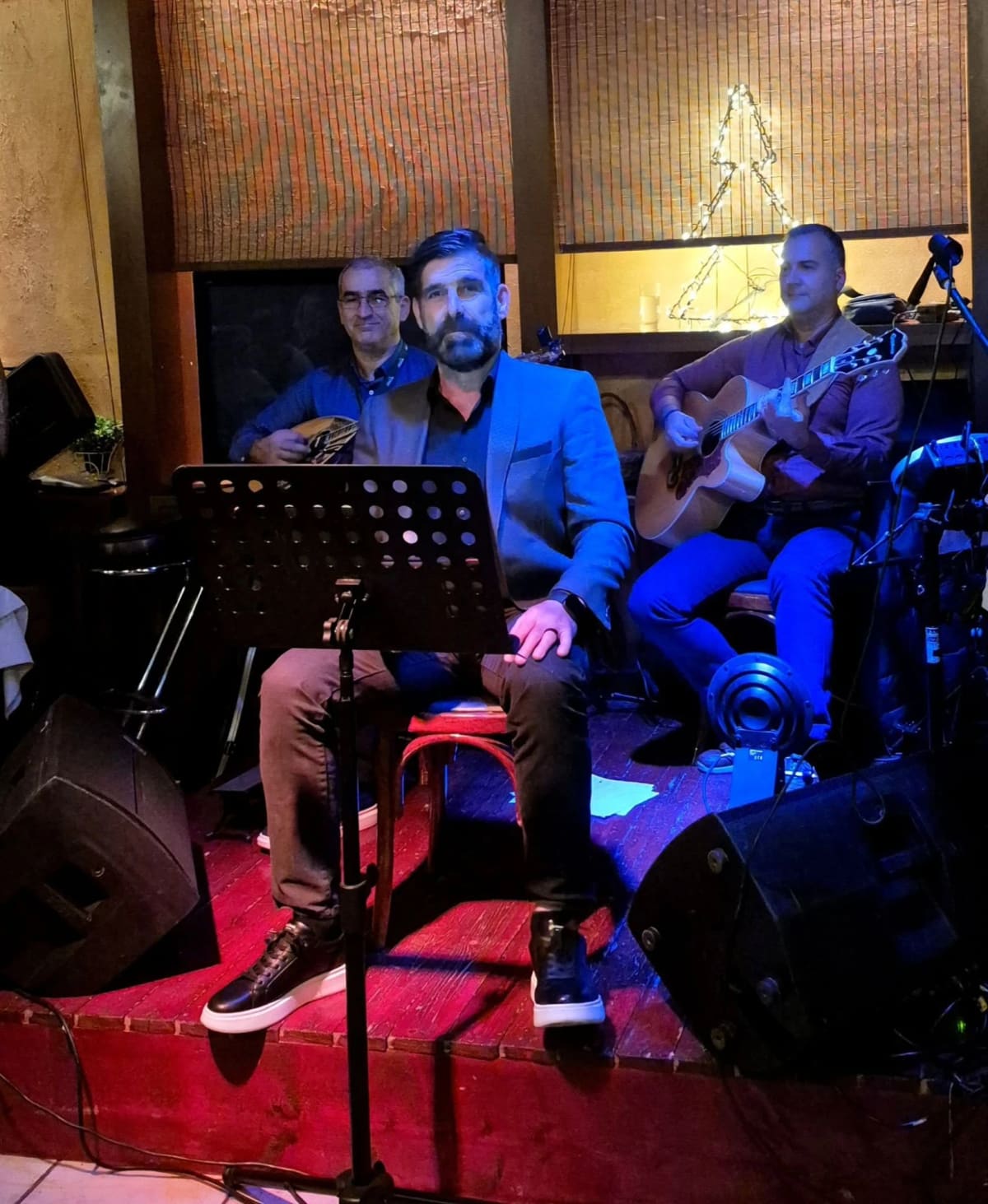 Three musicians on the small stage at Grammes: a singer behind a music stand, a bouzouki player and a guitarist