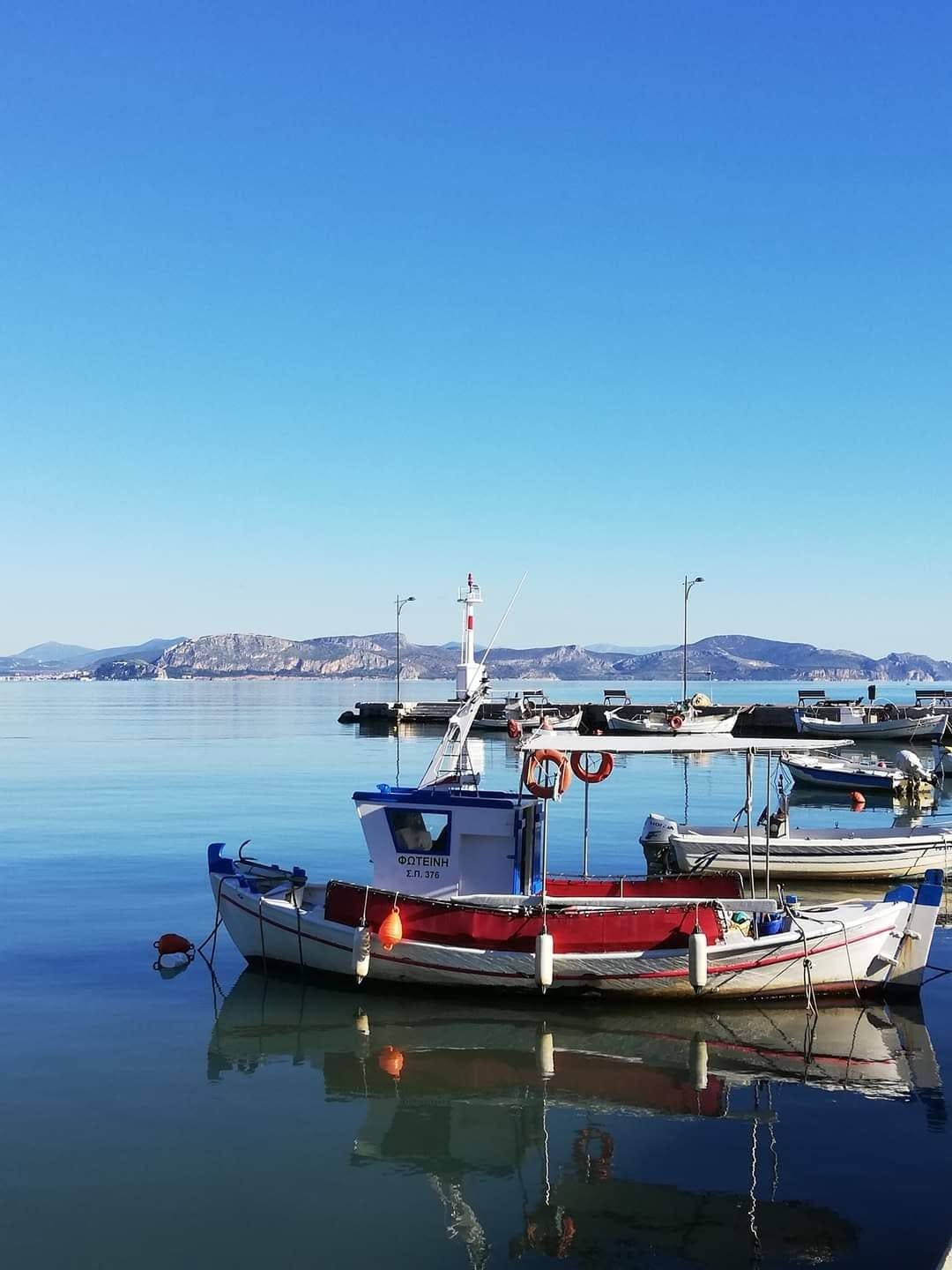 Small fishing boats reflected in the calm water of Myloi harbour under a clear blue sky