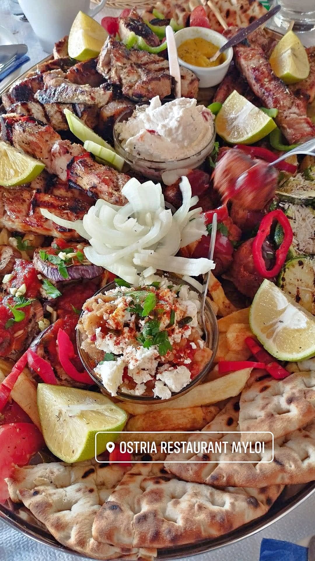 A large mixed platter with grilled meats, tzatziki, peppers, lemon and pitta bread