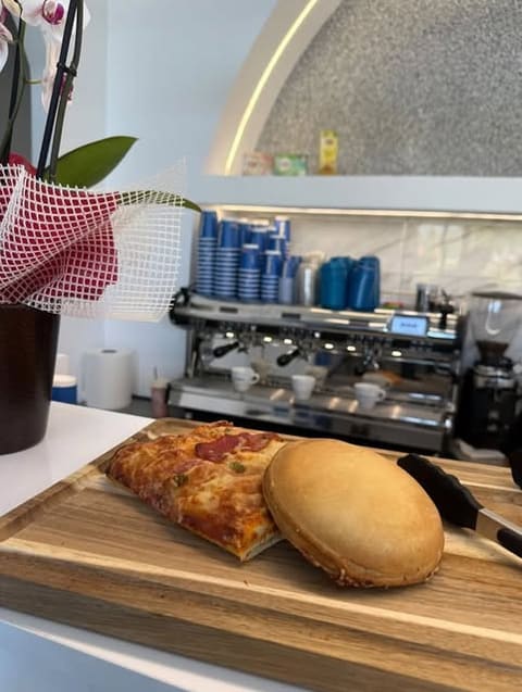 Espresso machine and coffee cups behind a wooden board with a pizza slice and a round pie