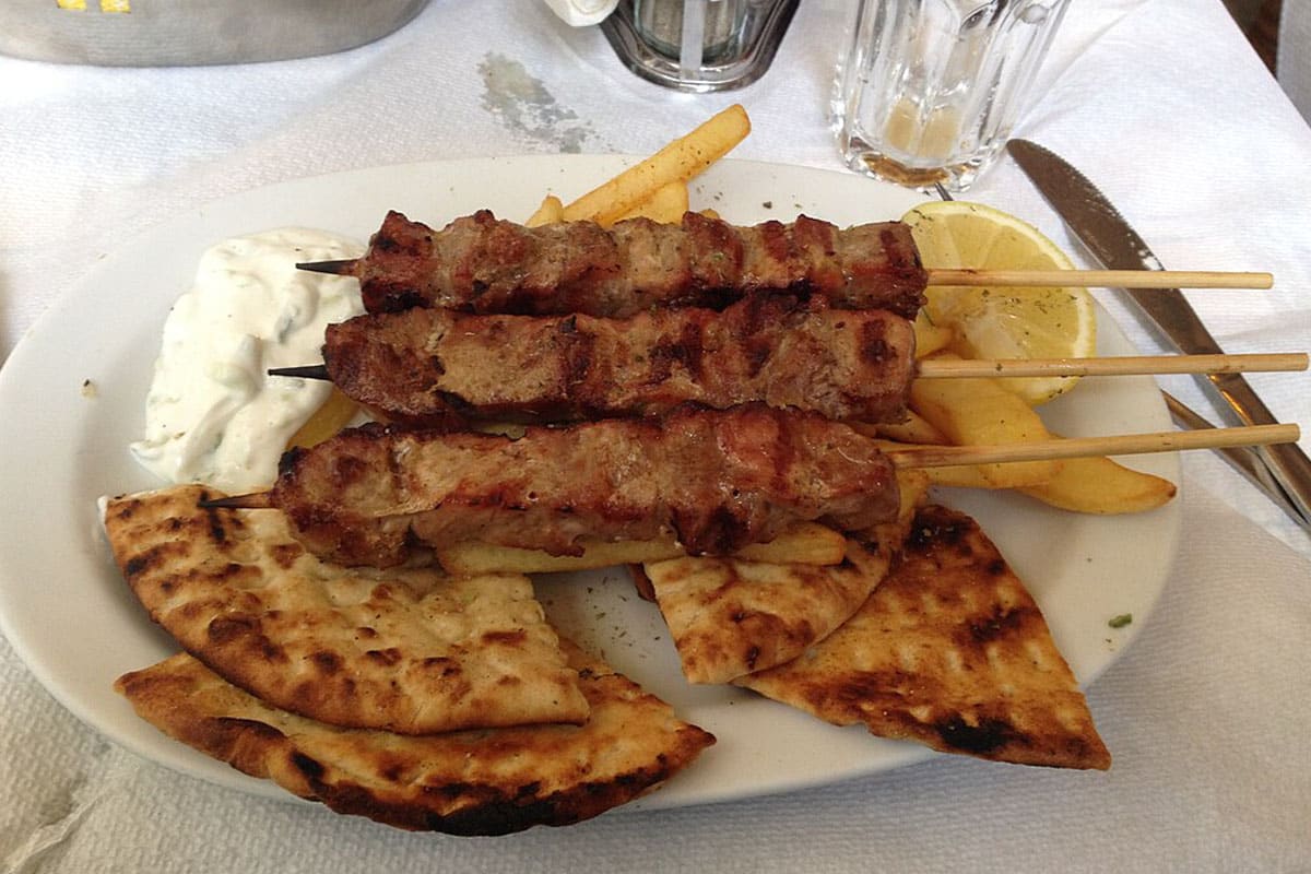 A plate of souvlaki skewers with grilled pita, fries and tzatziki