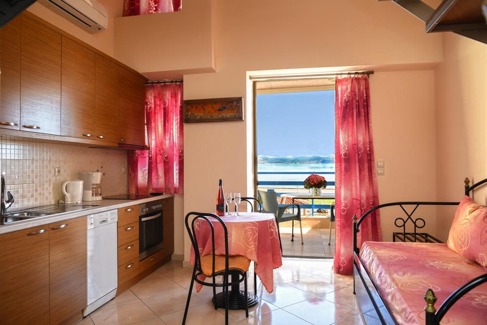 Kitchen with oven and hob, a small dining table and an open balcony door with a view of the sea