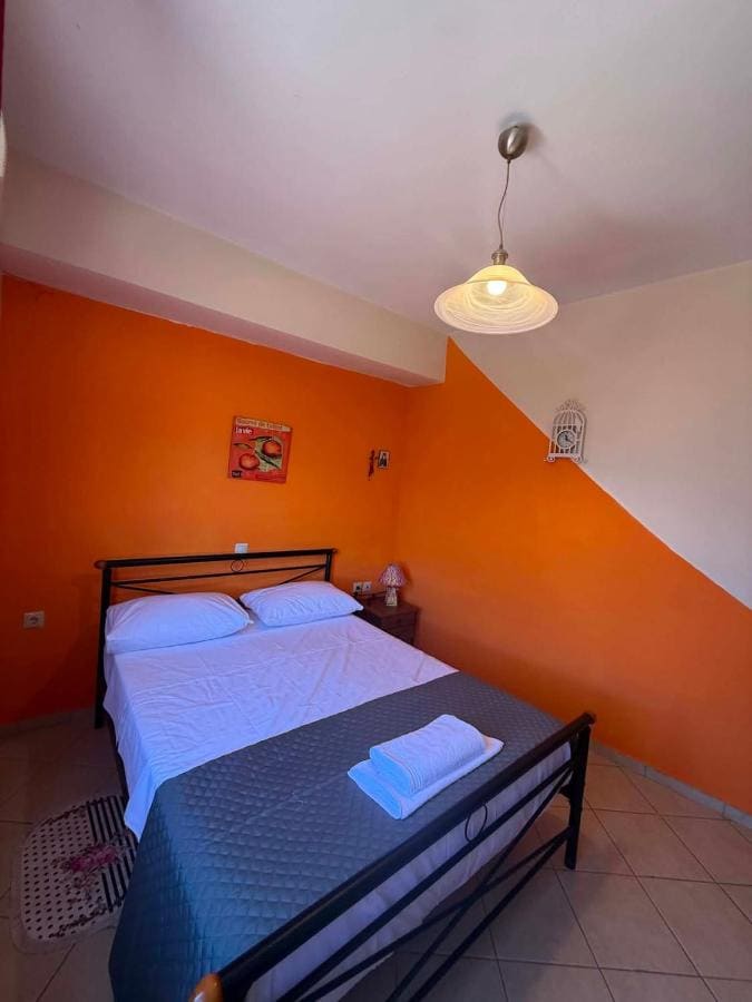 Bedroom with an orange wall, a double bed with a blue cover and folded towels