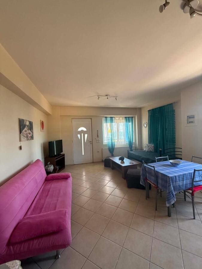 Living room with a pink sofa, a dining table with a blue checked cloth and windows with turquoise curtains