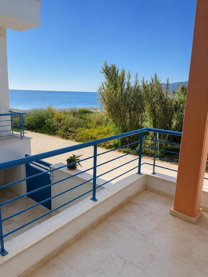 Balcony with blue railings above the garden, with reeds and the sea beyond