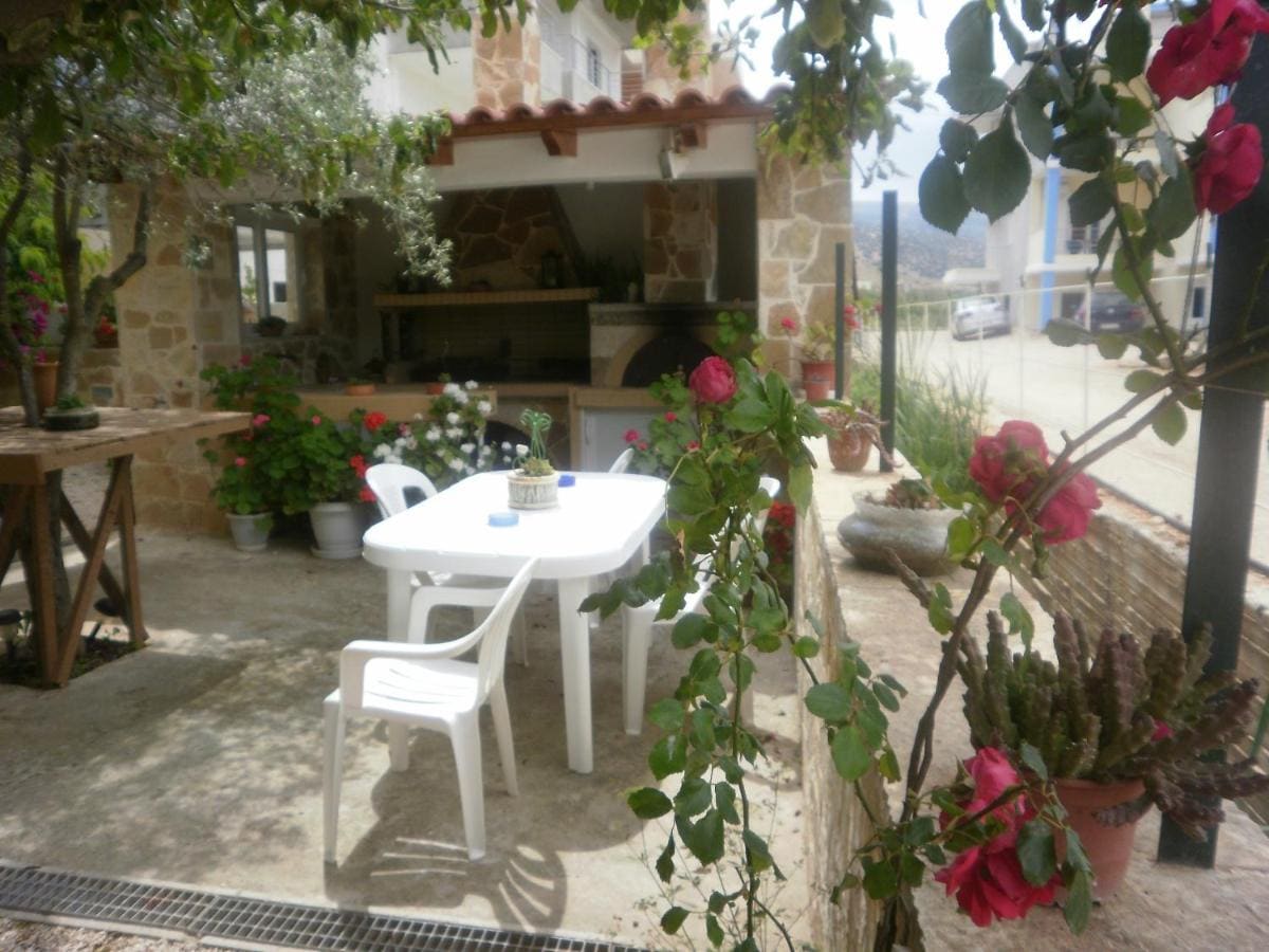 Shady courtyard with a white table and chairs, roses and plants, and a stone outdoor kitchen behind
