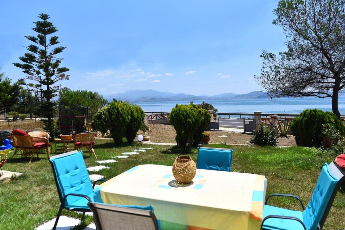 Garden table with blue chairs on the lawn, with trees, the sea and the mountains beyond
