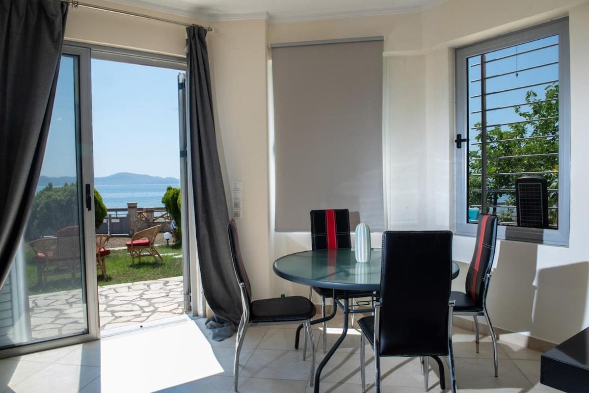 Round glass dining table with black chairs by the open sliding door, with the garden and the sea outside