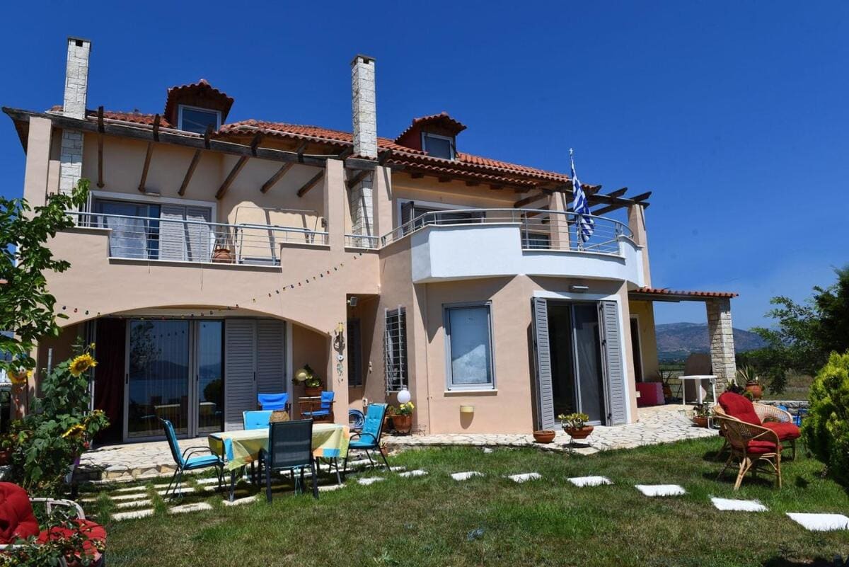 The two-storey house with tiled roofs, balconies and a garden with a table and chairs in front
