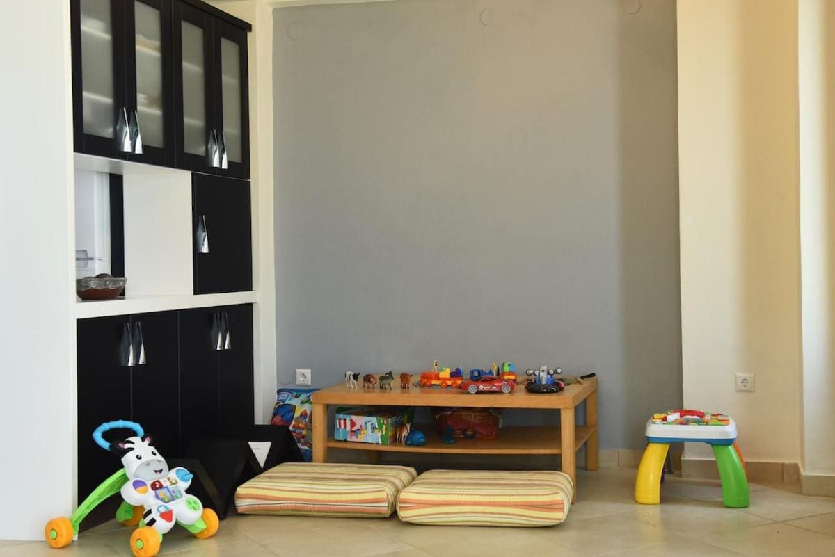 Play corner with a low table full of toys, floor cushions and a baby walker
