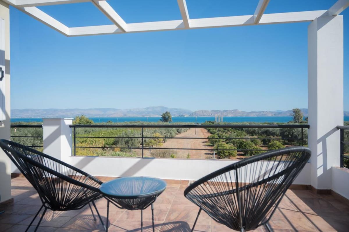 Balcony under a pergola with two chairs, looking out over olive groves to the sea and mountains