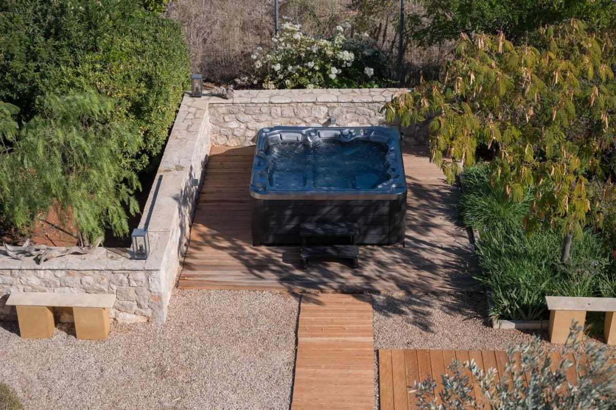 Hot tub set among garden plants, reached by a wooden path between stone walls