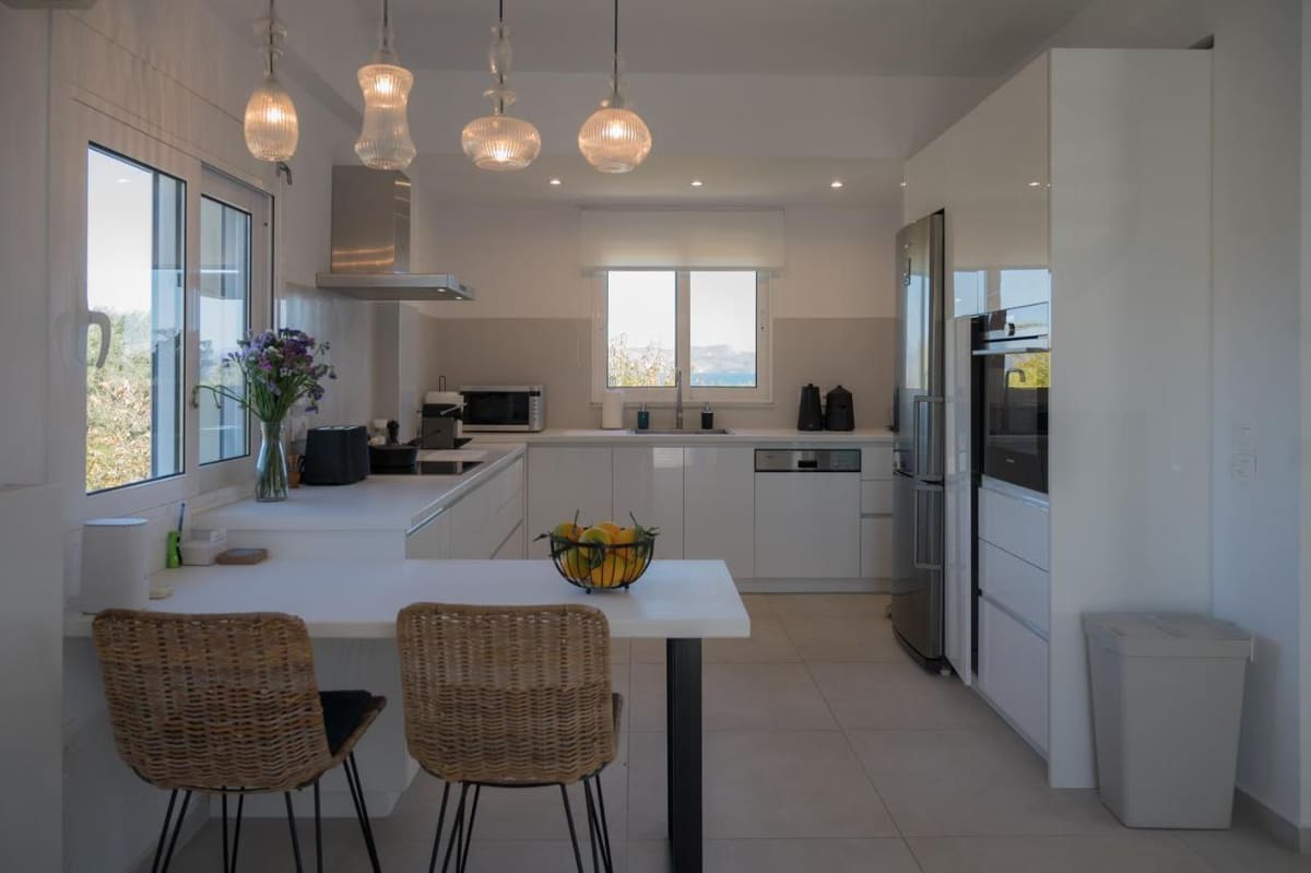 White fitted kitchen with pendant lamps, a breakfast bar and rattan stools
