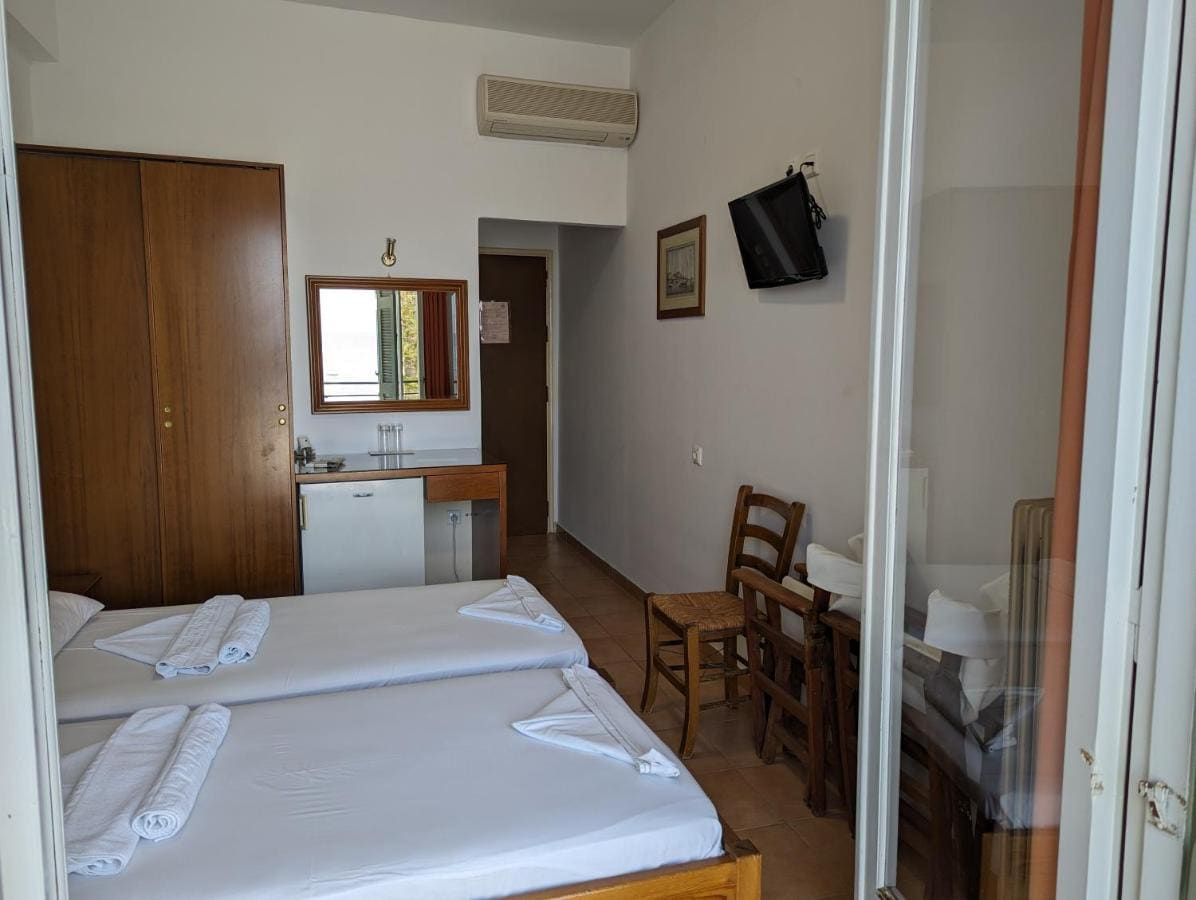 Room with two single beds, a wooden wardrobe, a TV and a door to the balcony
