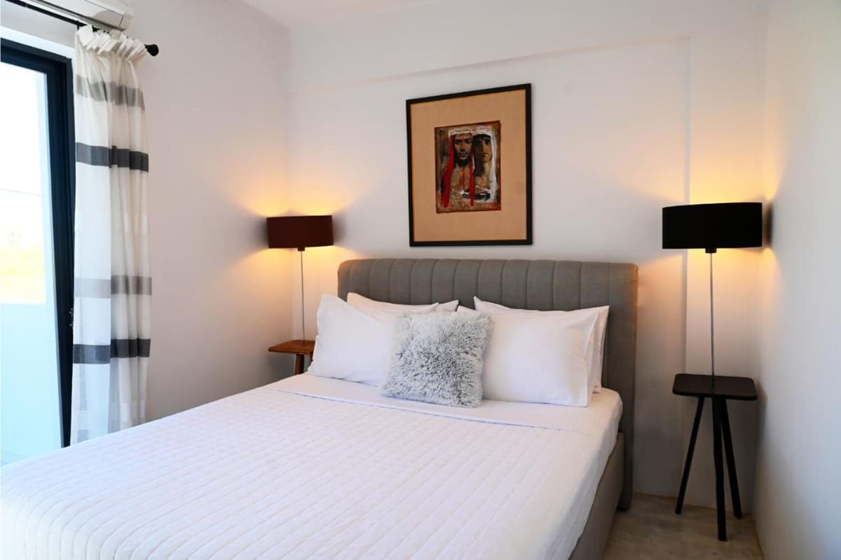 Bedroom with a double bed, white linen, a grey upholstered headboard and black floor lamps on both sides