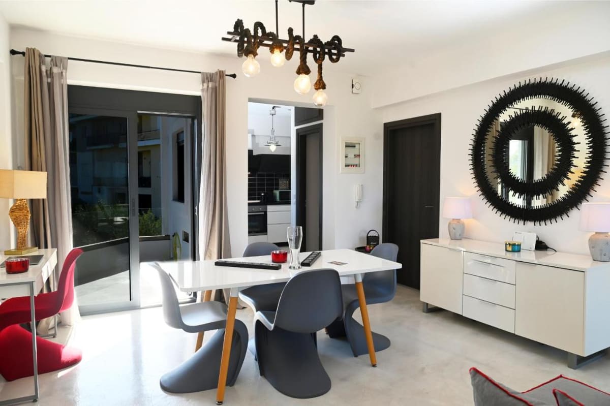 Dining area with a white table, grey and red designer chairs, a decorative chandelier and a large round mirror