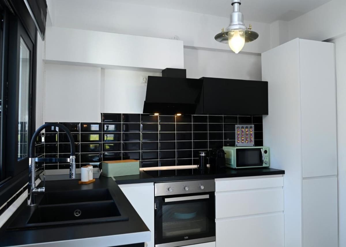Fitted kitchen with black tiles, a black hood, an oven, a microwave and white cabinets