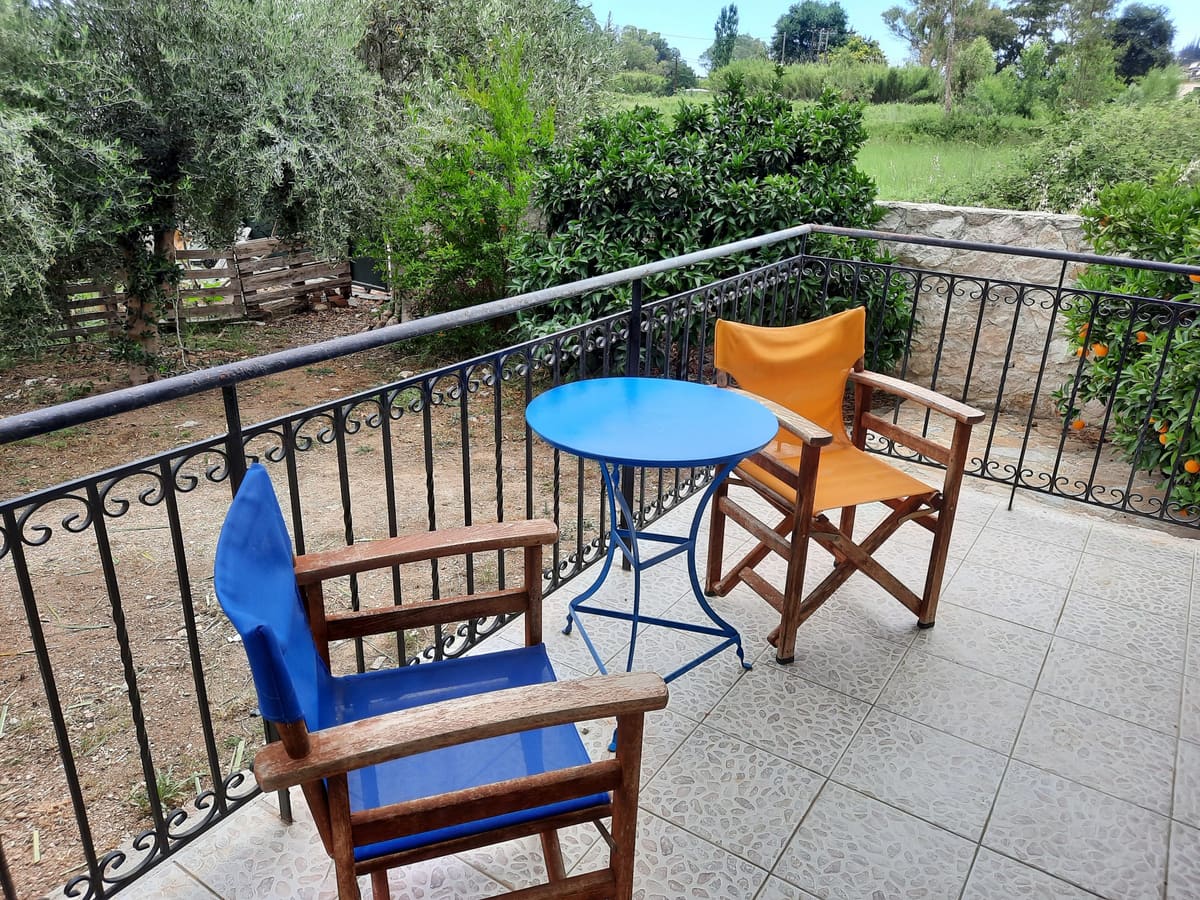Balcony with blue and orange director's chairs and a round blue table, looking out over the garden trees