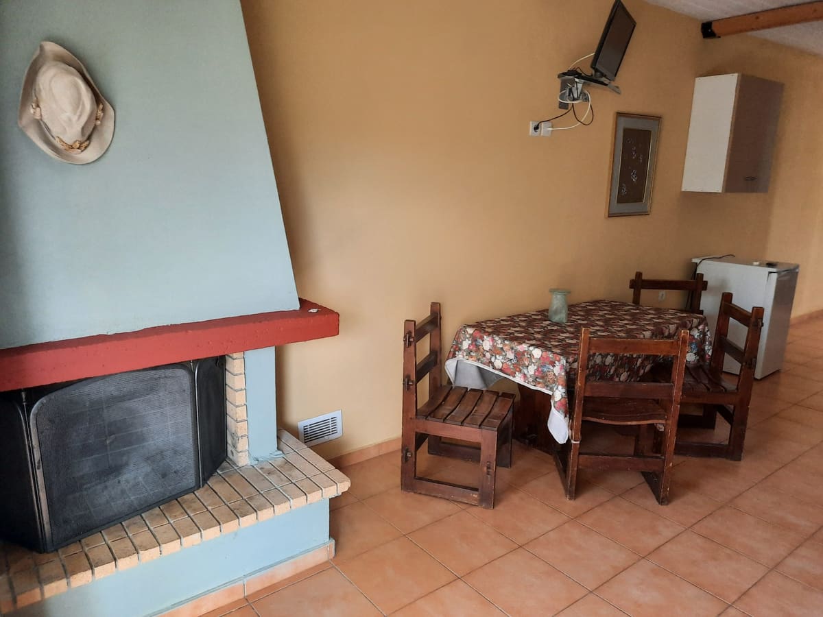 Living area with a white corner fireplace, a wooden dining table with chairs and a beamed ceiling