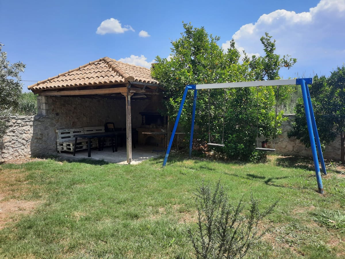 The large garden with a lawn, a covered barbecue corner and blue swings among orange trees