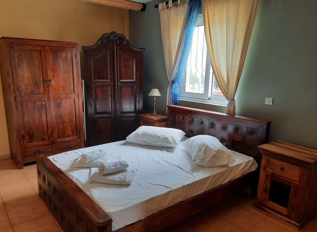 Bedroom with a tall wooden wardrobe, a double bed with folded towels and a window with curtains