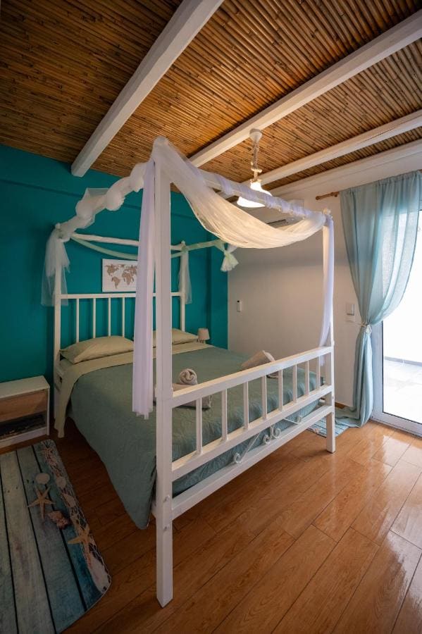 Bedroom with a white four-poster bed, a turquoise wall, a wooden floor and light curtains