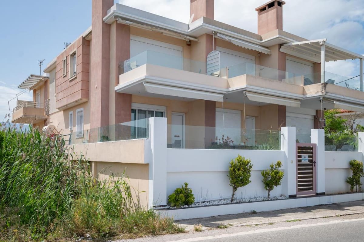 The house from the street: pink and white walls, glass balconies with awnings, and a white garden wall with small trees