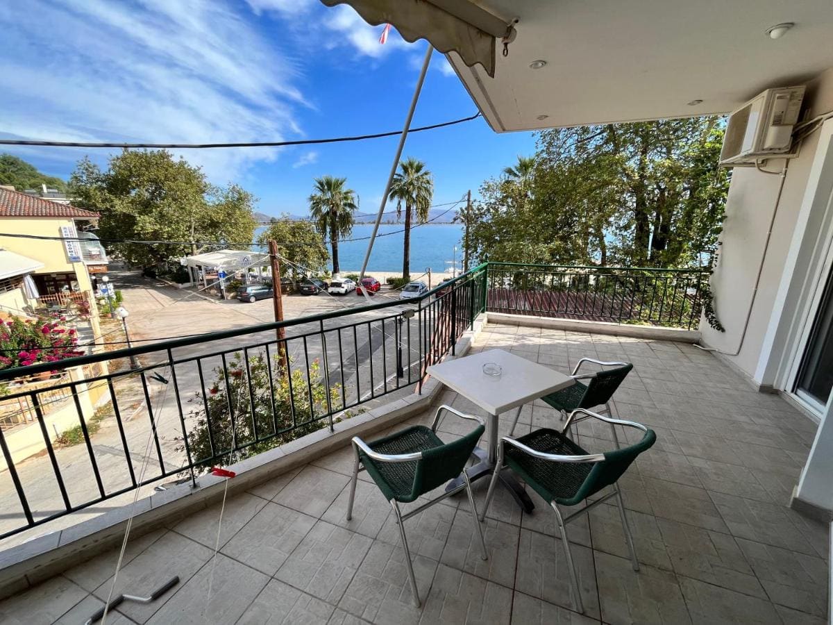 Large balcony with a table and green chairs, looking over the street, trees and palms to the sea