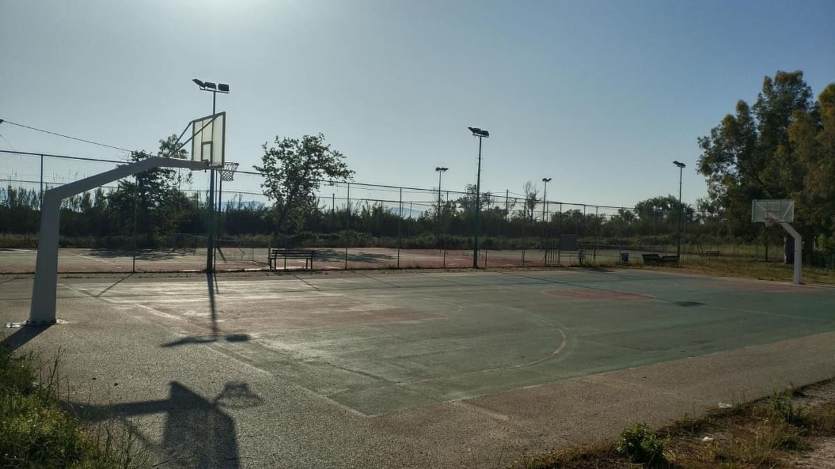 The tennis court with its nets and lights, among trees under a bright sky