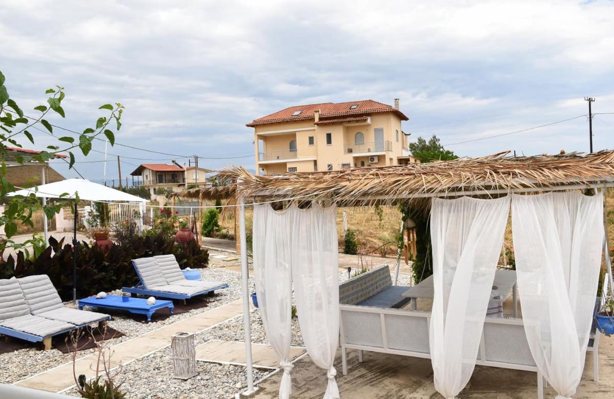 Garden lounge under a reed pergola with white curtains, blue and white sun loungers and a gravel garden
