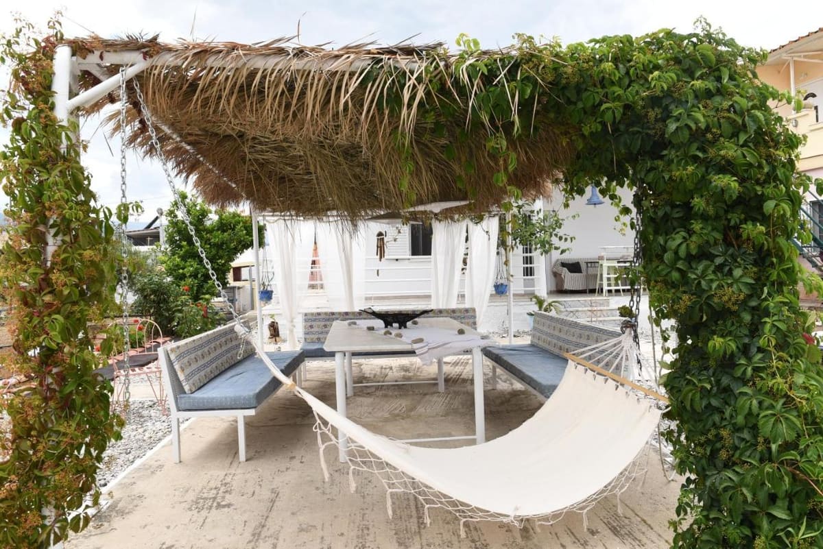 A white hammock under a pergola overgrown with green climbers