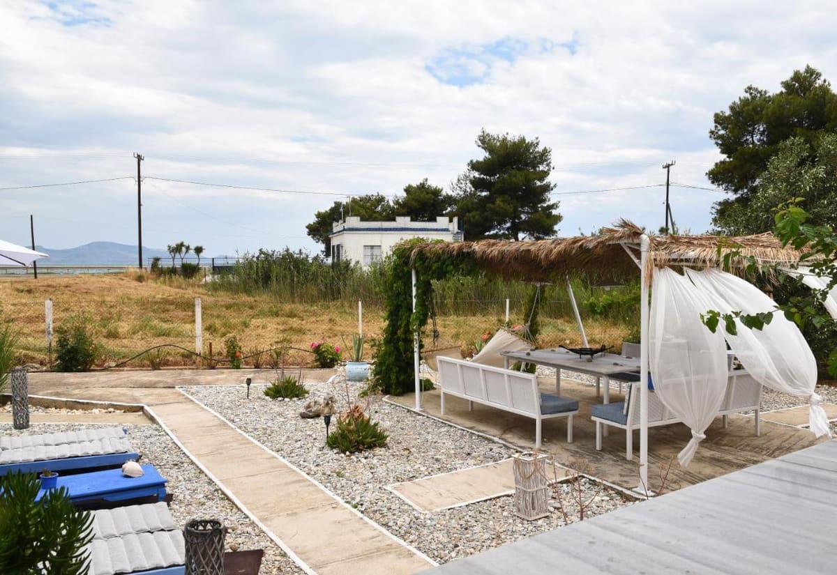 Outdoor seating with white sofas under a pergola, with the sea and mountains in the distance