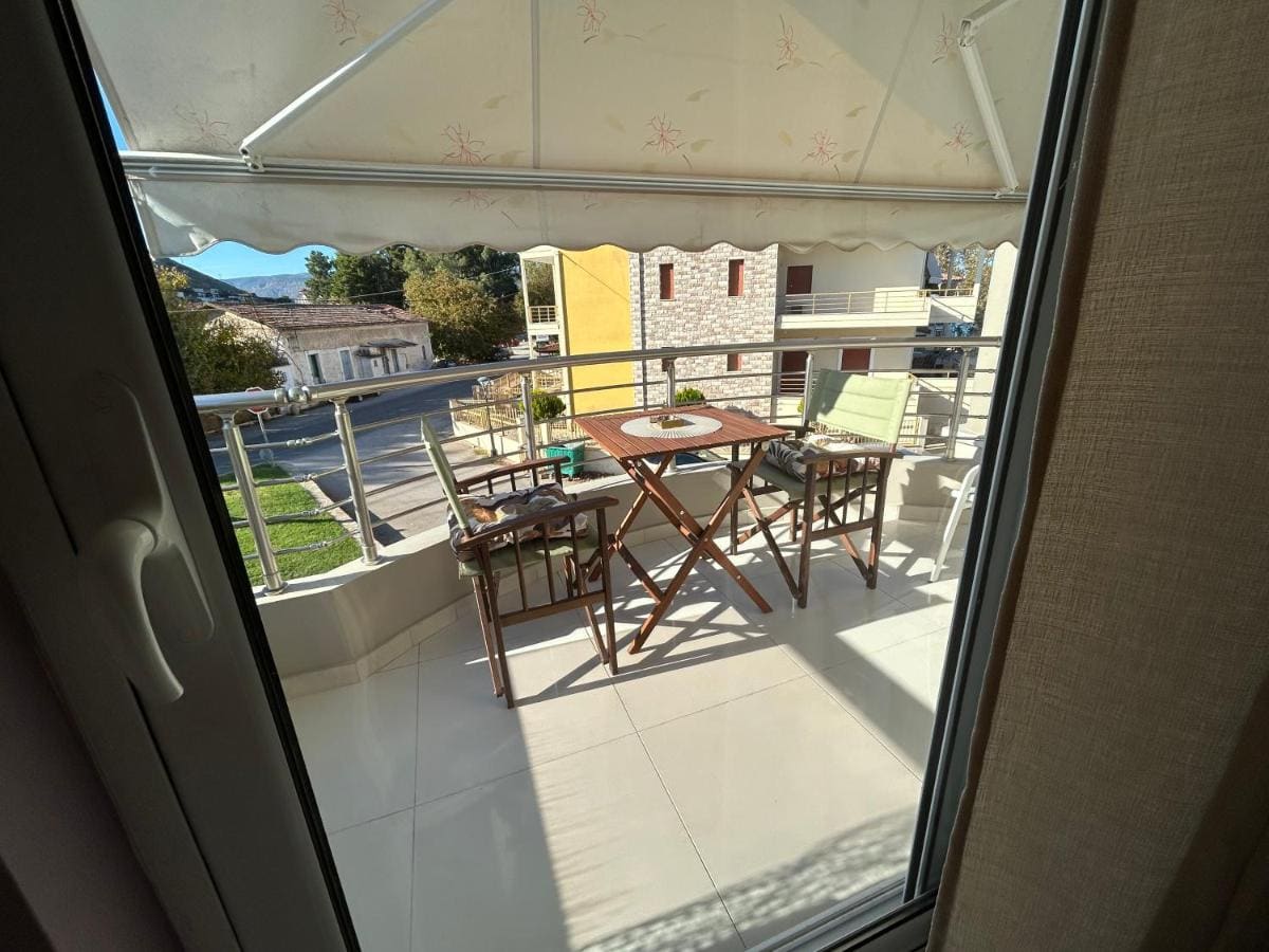 Covered balcony with a wooden table and chairs under an awning, seen through the open balcony door