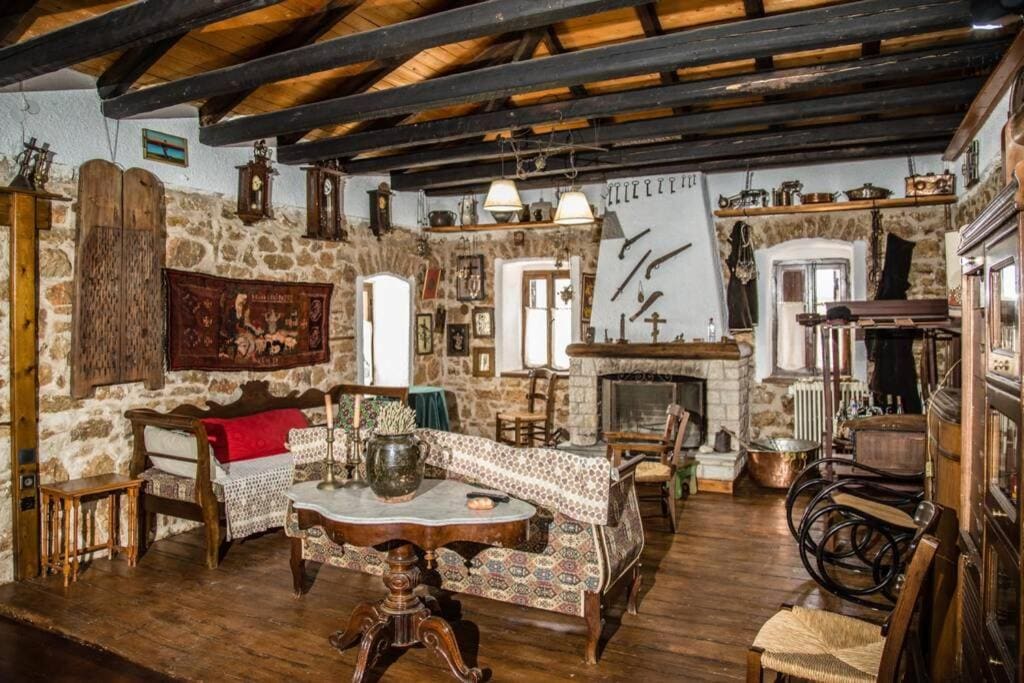 Living room with stone walls, dark wooden beams, a fireplace, old furniture, rugs and family heirlooms