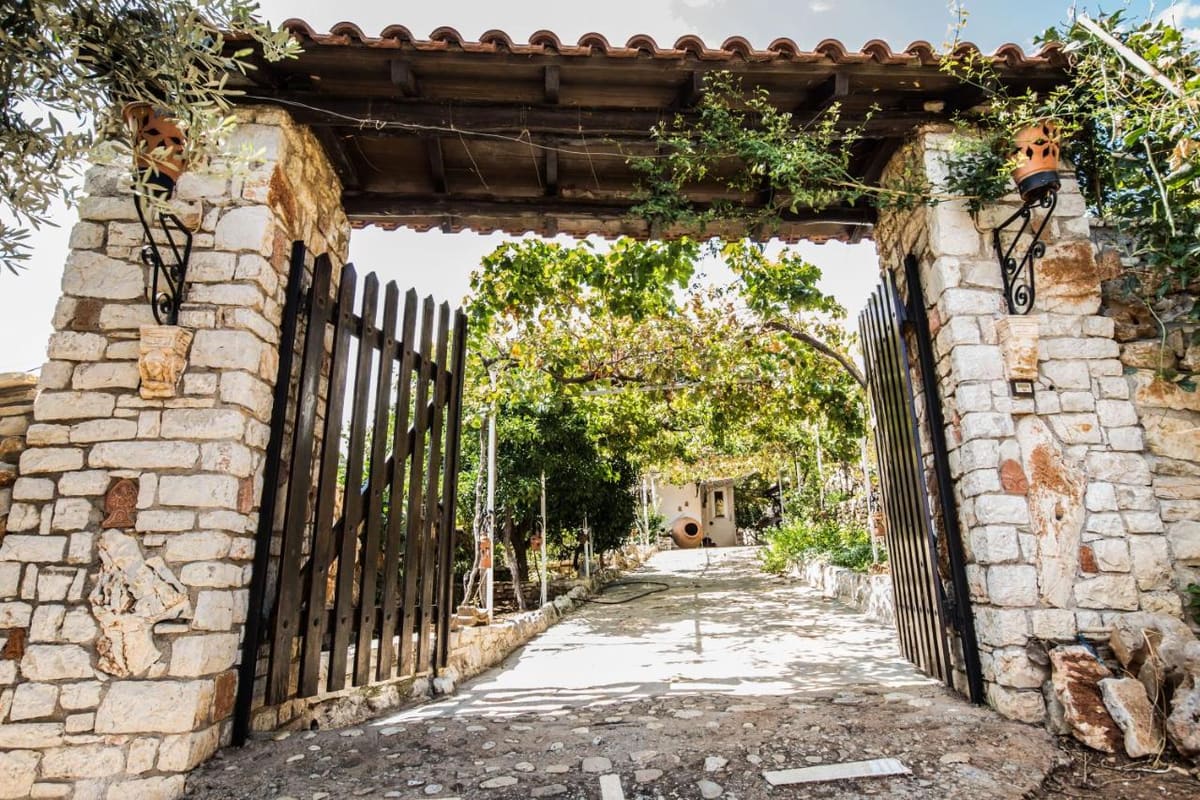 Stone gateway with a tiled roof and an open wooden gate onto a shady garden path
